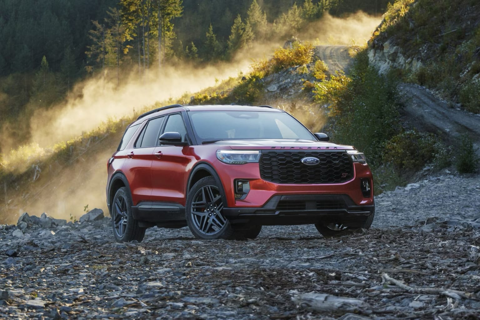 An SUV navigating a rocky, dusty path surrounded by forested hills.