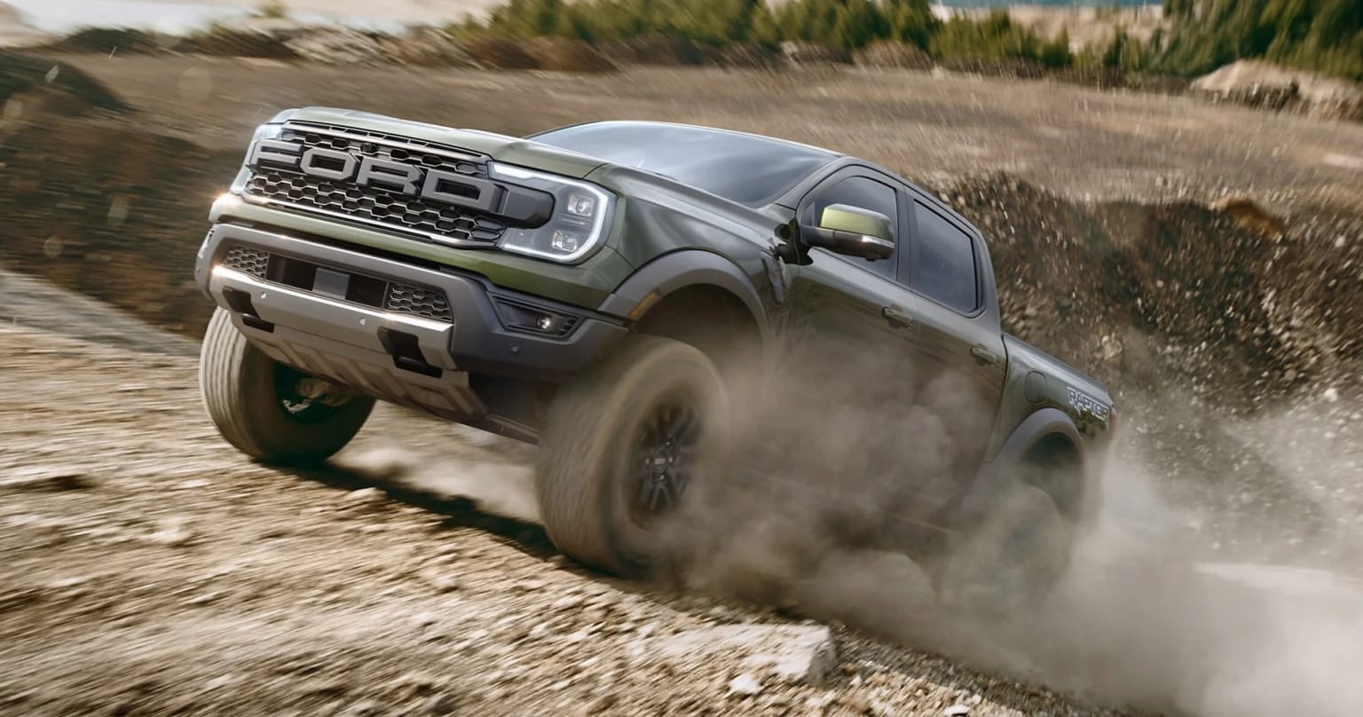 Off-road vehicle driving through dusty, rocky terrain kicking up dust.