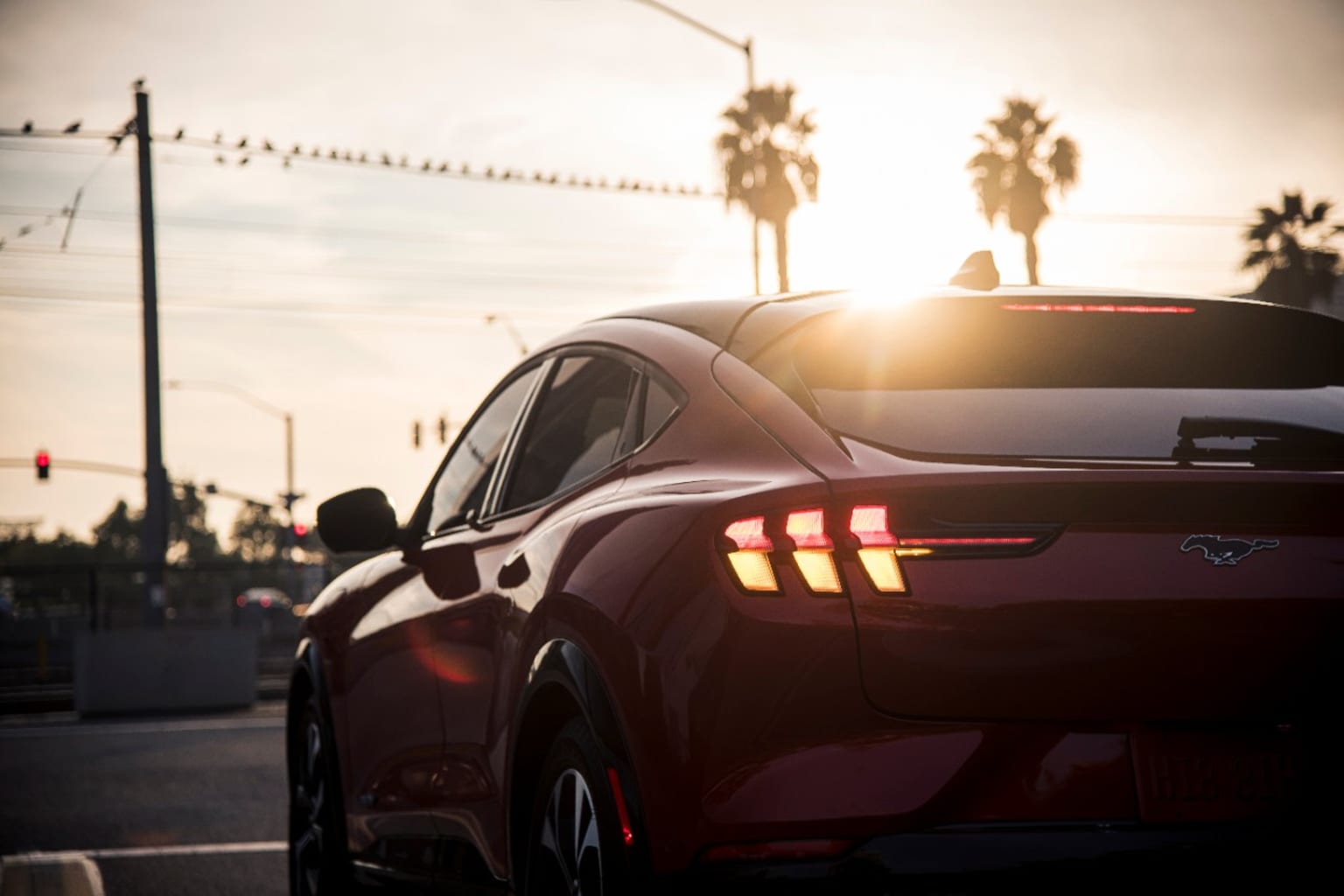 a red car driving down a street next to a palm tree lined street at sunset with the sun shining on the back of the car