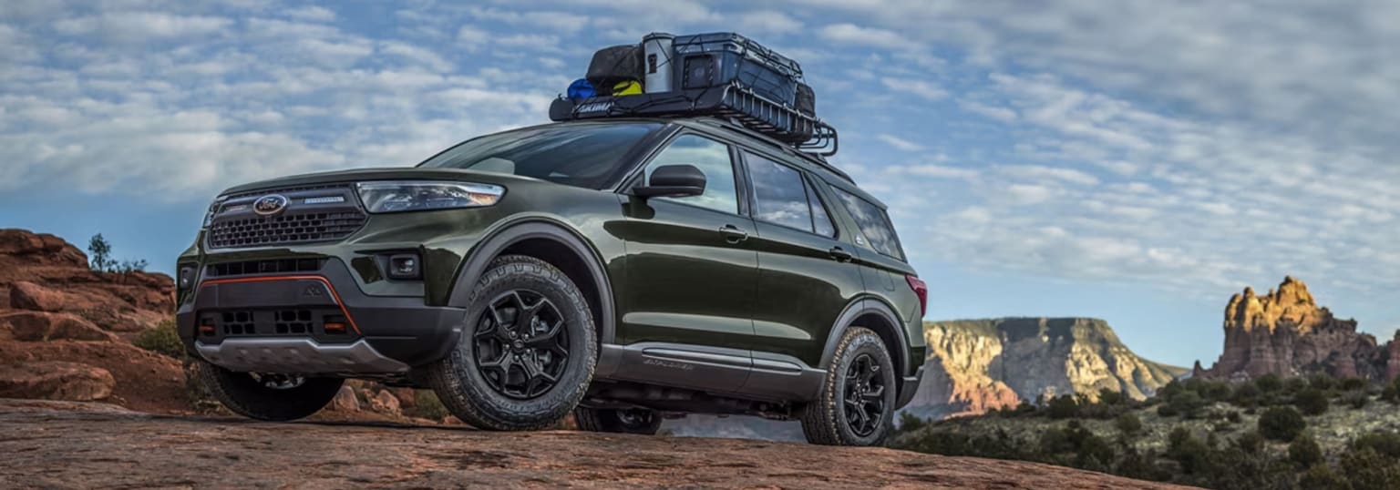 Off-road vehicle with a cargo carrier on roof in scenic outdoor setting with mountainous landscape visible in background.