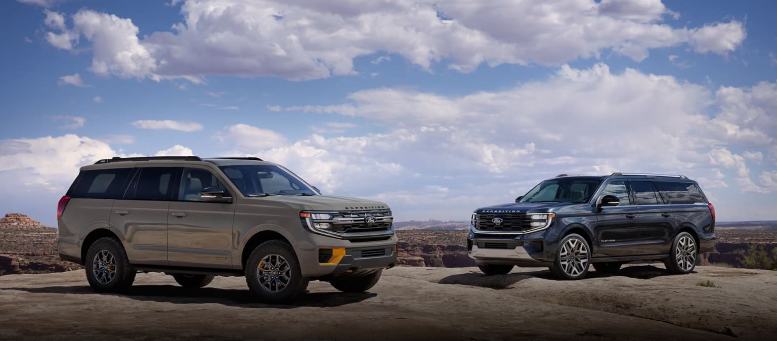Two rugged SUVs parked on rocky desert terrain with a cloudy blue sky in the background.