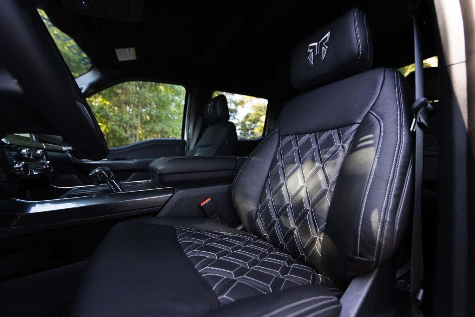 Interior image of a vehicle with black leather seats featuring a diamond-patterned design. The background outside the vehicle is blurred, suggesting a natural setting.