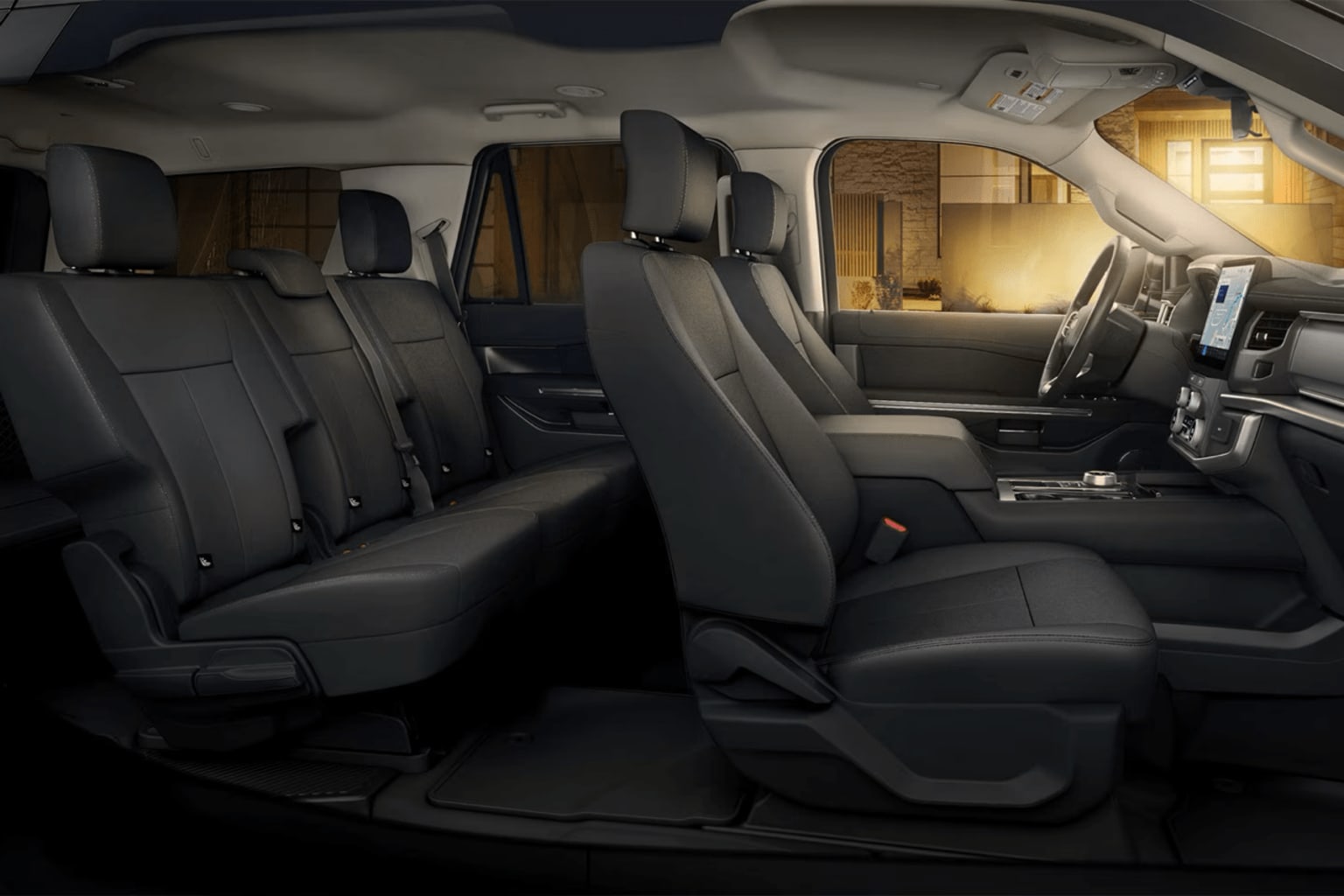 Interior of a vehicle with multiple rows of black leather seats and a dimly lit background visible through the windshield.