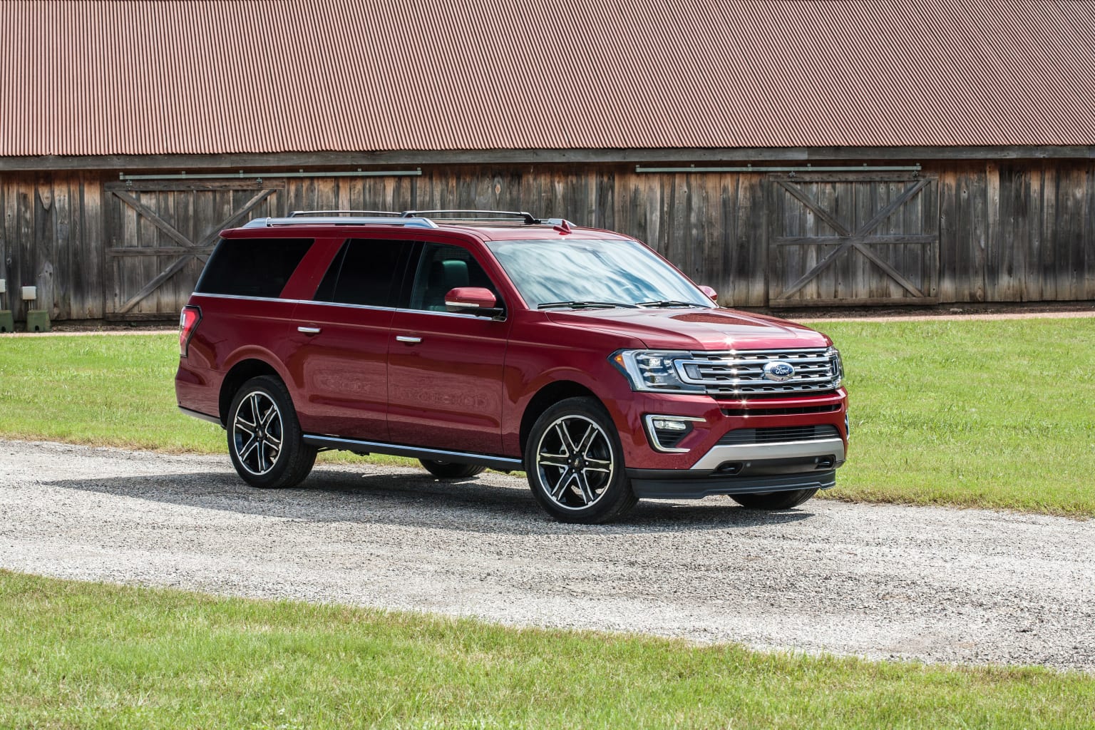 a red ford expedition vehicle parked on a gravel road in front of a barn with a barn in the background