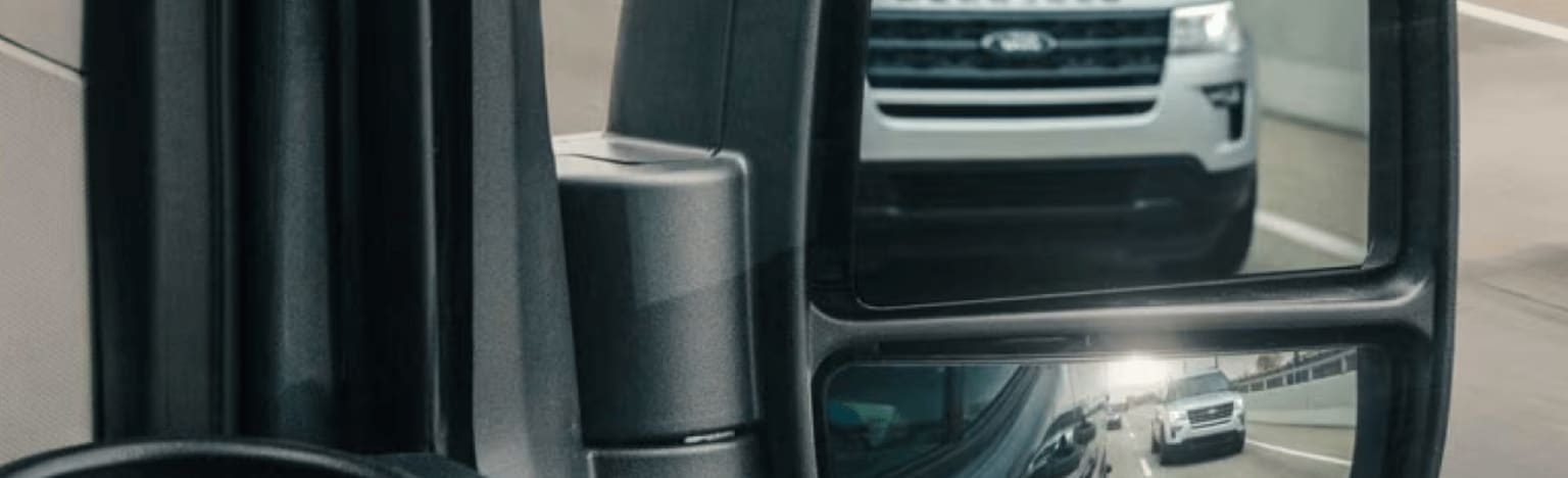 A silver SUV is reflected in the side mirror of a vehicle, with other cars visible in the distance.