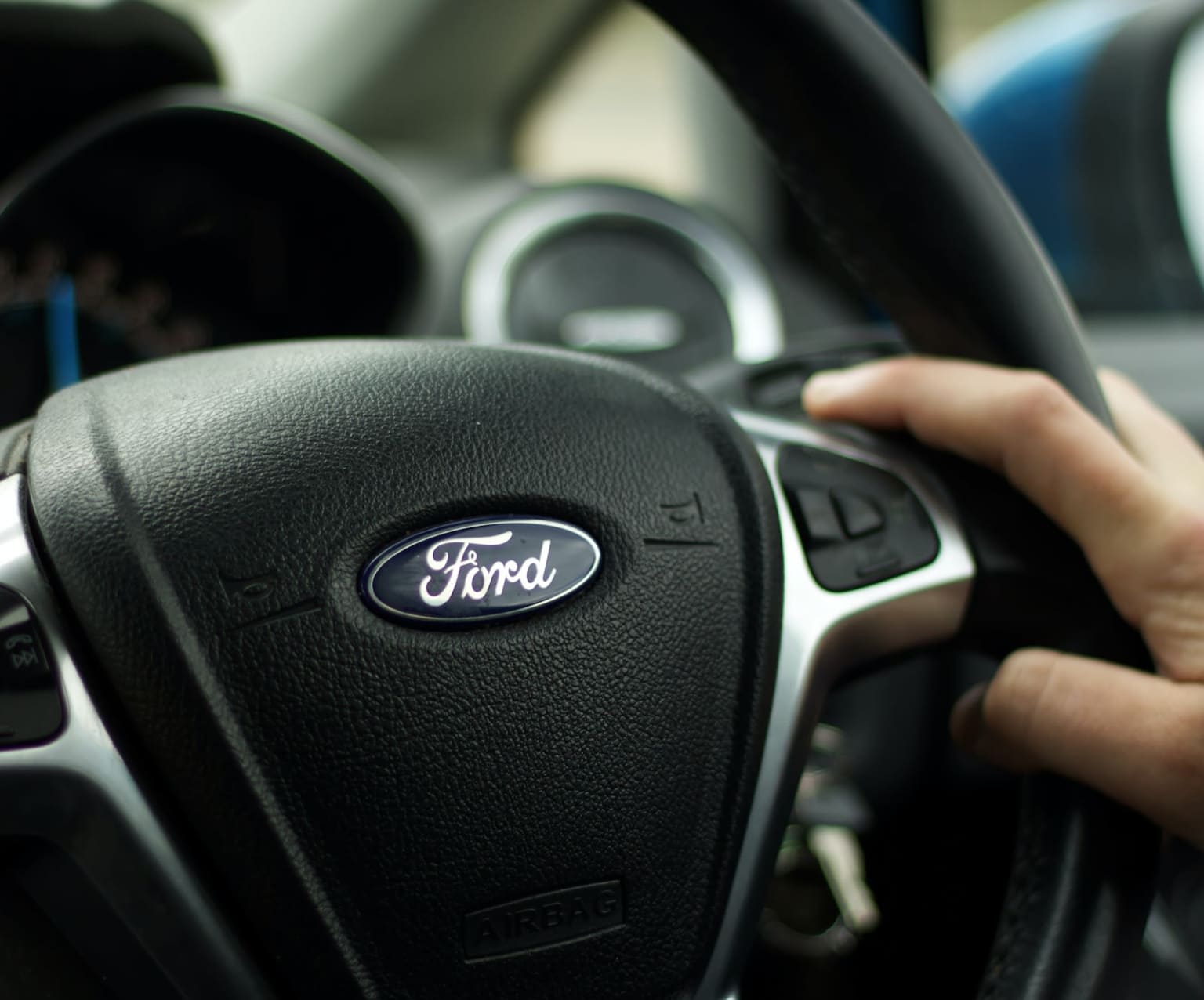 a close up of a person driving a car with a steering wheel and a hand on the steering wheel