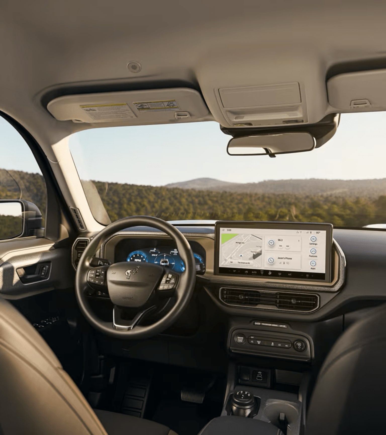Interior of a vehicle with dashboard display and steering wheel, overlooking a scenic landscape.