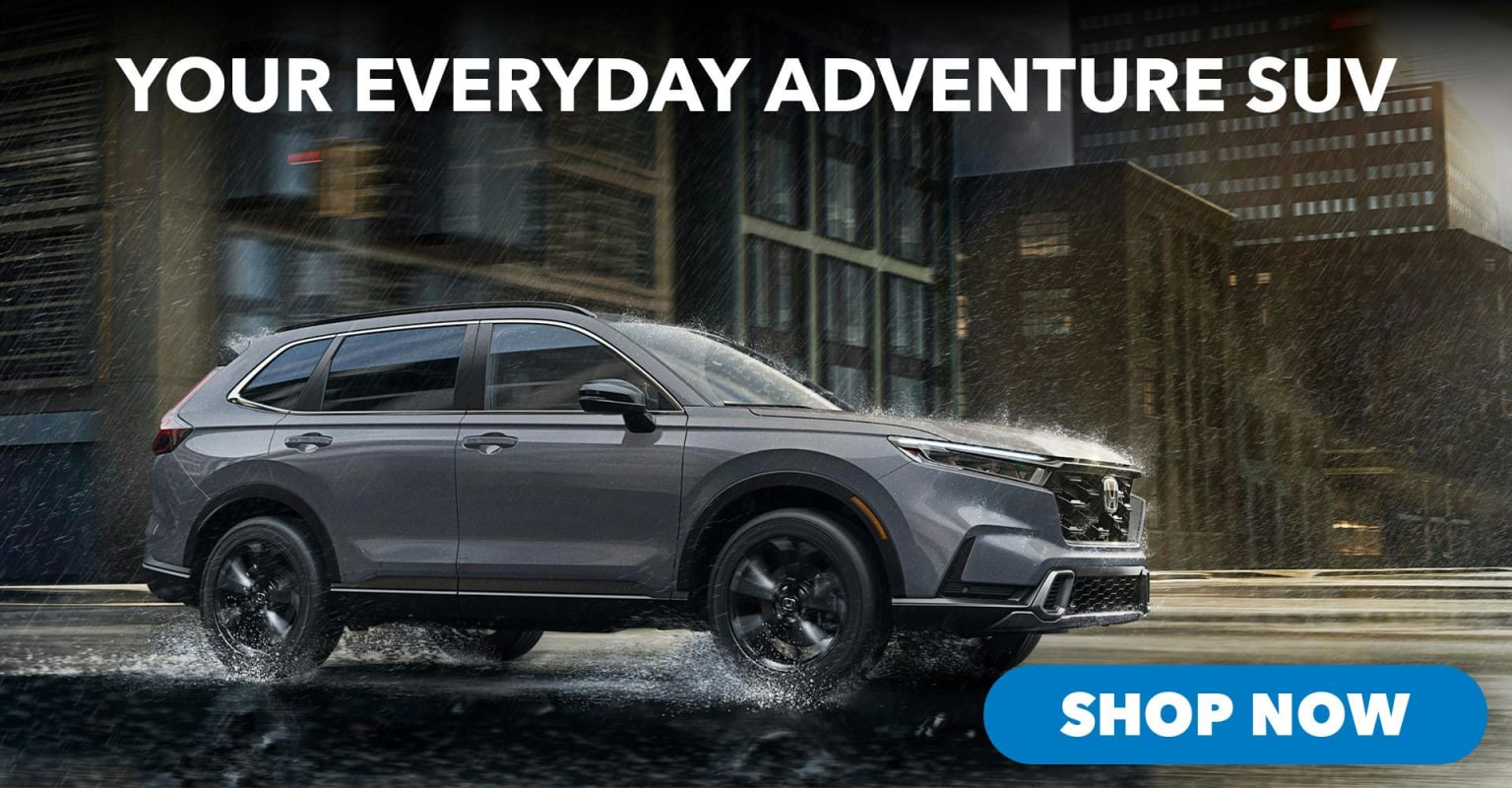 A gray SUV driving through a wet city street with tall buildings in the blurred background.