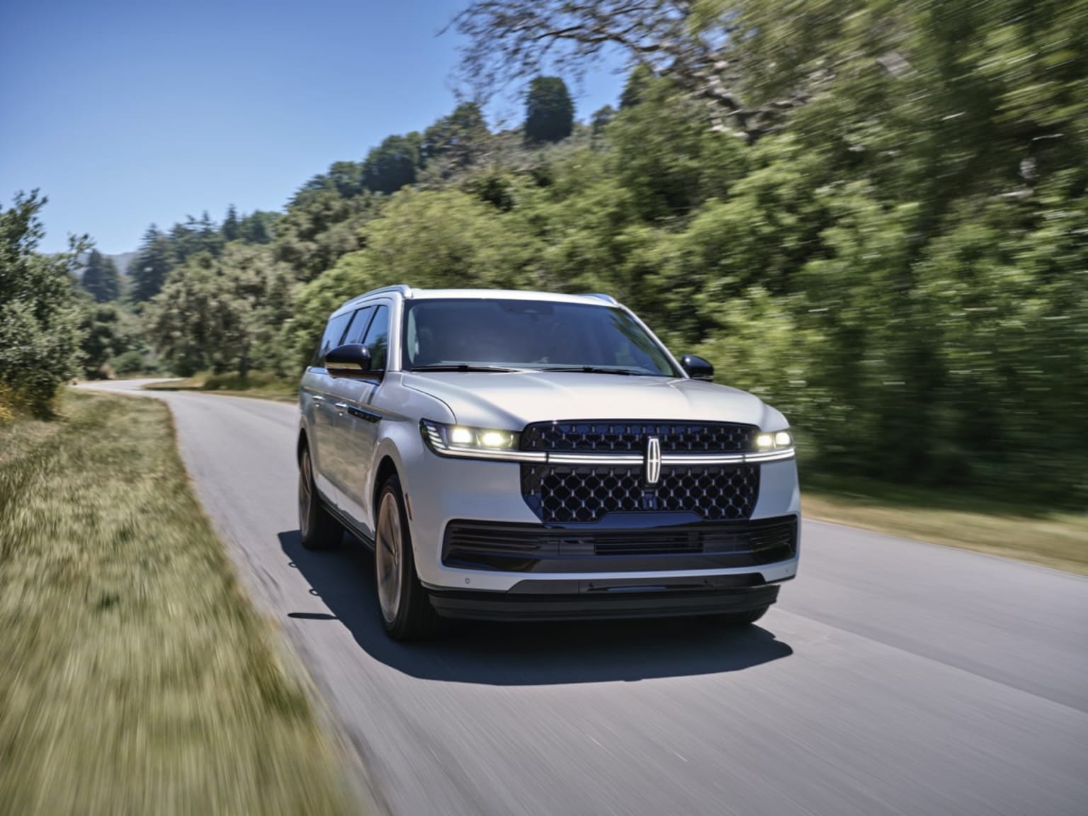 A silver SUV on a winding road surrounded by lush foliage and a clear blue sky.