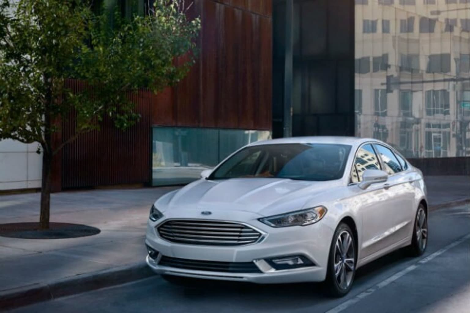 a white car driving down a street next to a tall building with a clock on it's side
