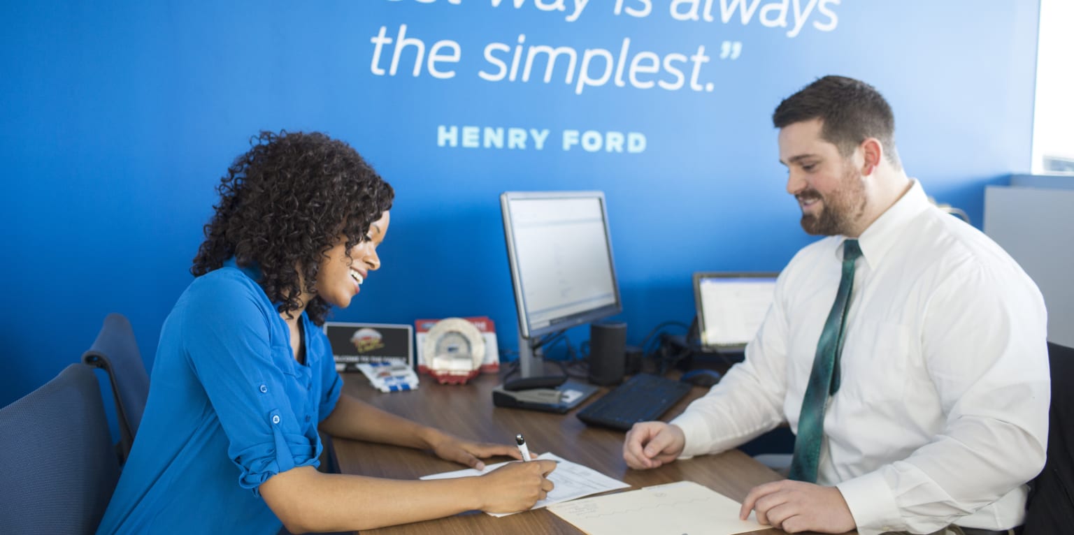 a man and a woman sitting at a desk with a notepad and pen in front of a blue wall