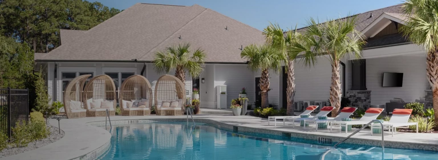 a swimming pool with lounge chairs and palm trees in front of a white house with a large swimming pool