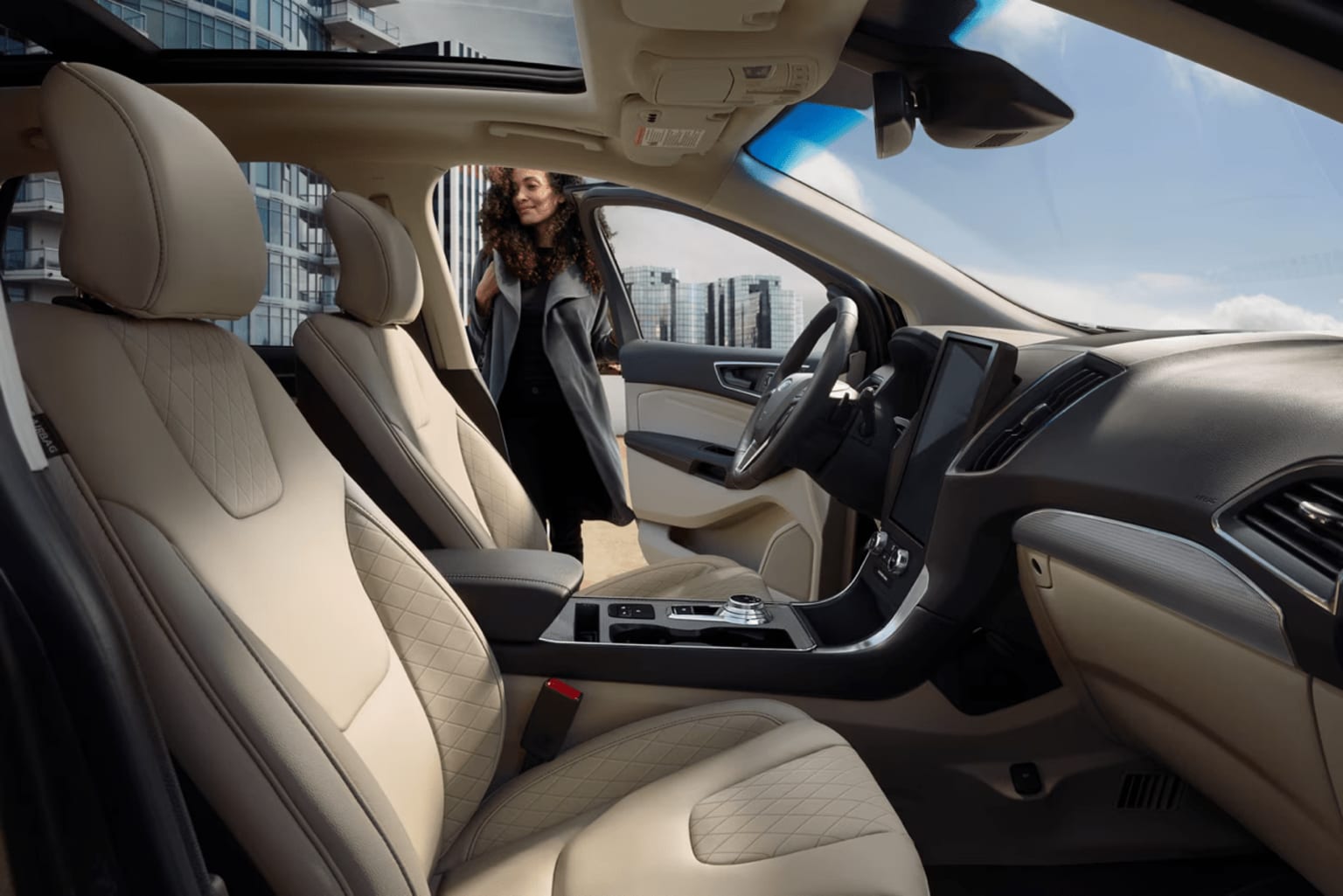 The image shows the interior of a vehicle with a person sitting in the driver's seat and the cityscape visible through the windshield in the background.