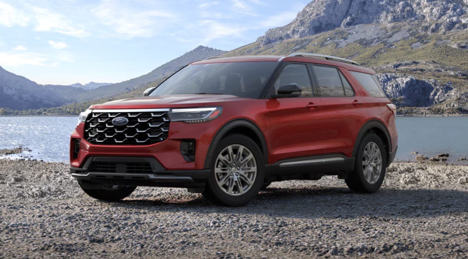 Red SUV parked on a rocky shore with mountainous landscape in the background.
