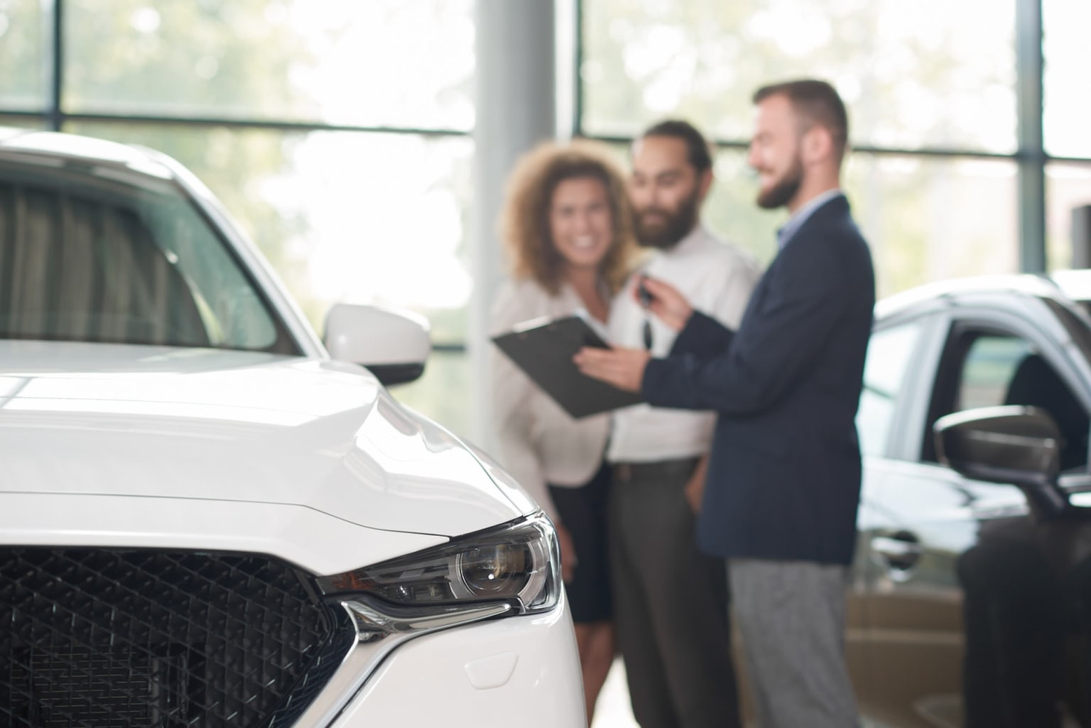 a man and a woman standing in front of a car in a dealership looking at a clipboard