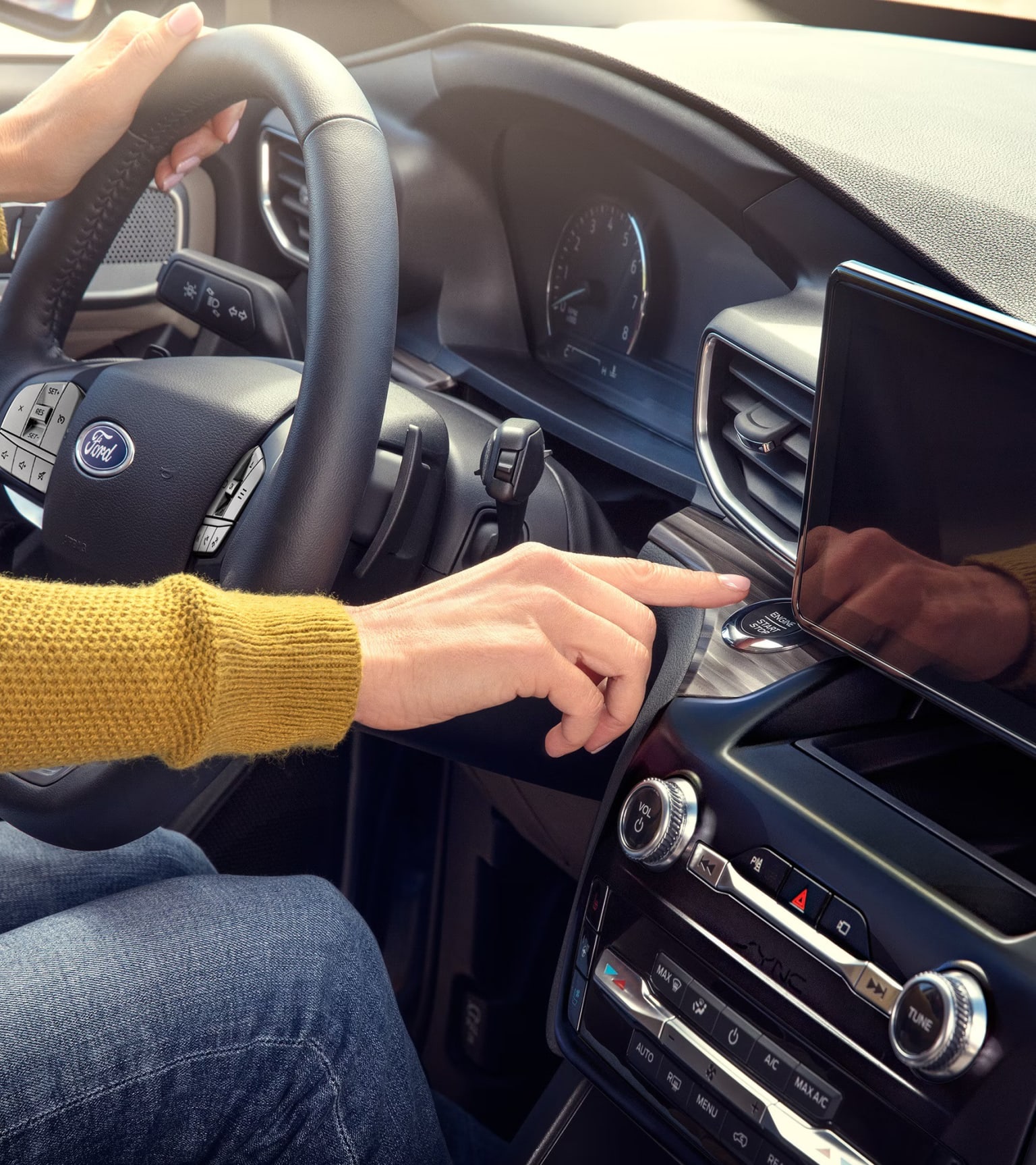 A person's hands are on the steering wheel and pressing a button in a modern car interior with a large touchscreen display.