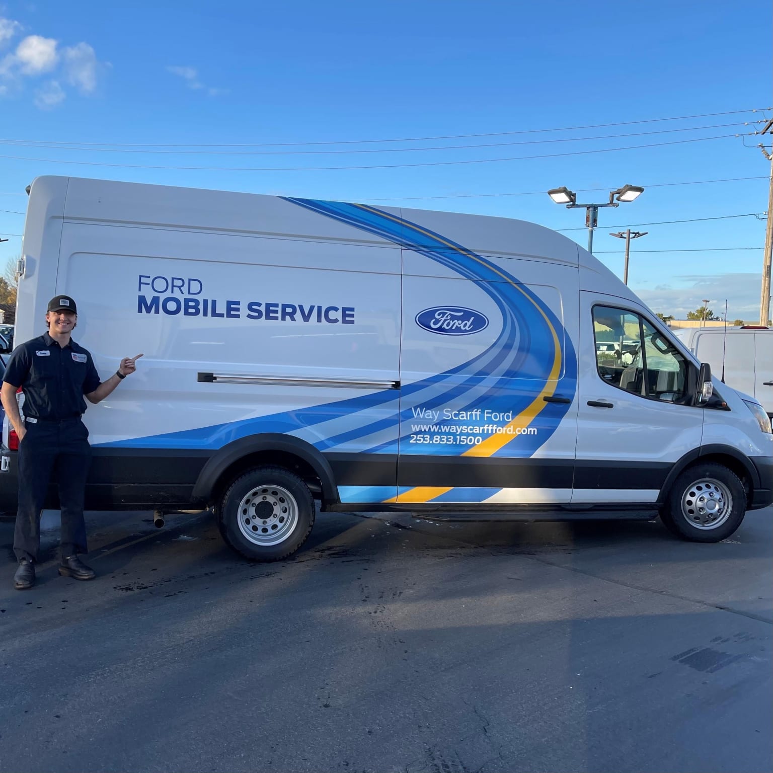 A mobile service van parked on a paved surface, with a blue sky and some buildings visible in the background.