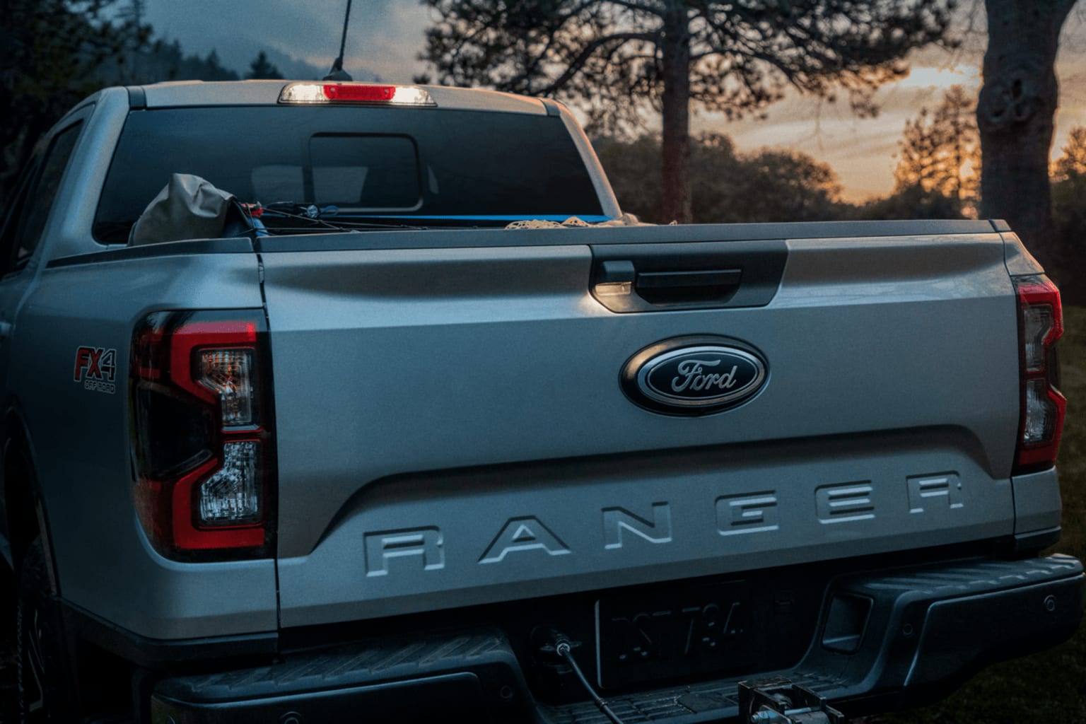 A silver pickup truck with the "Ranger" text visible on the tailgate, set against a backdrop of trees and a sunset sky.