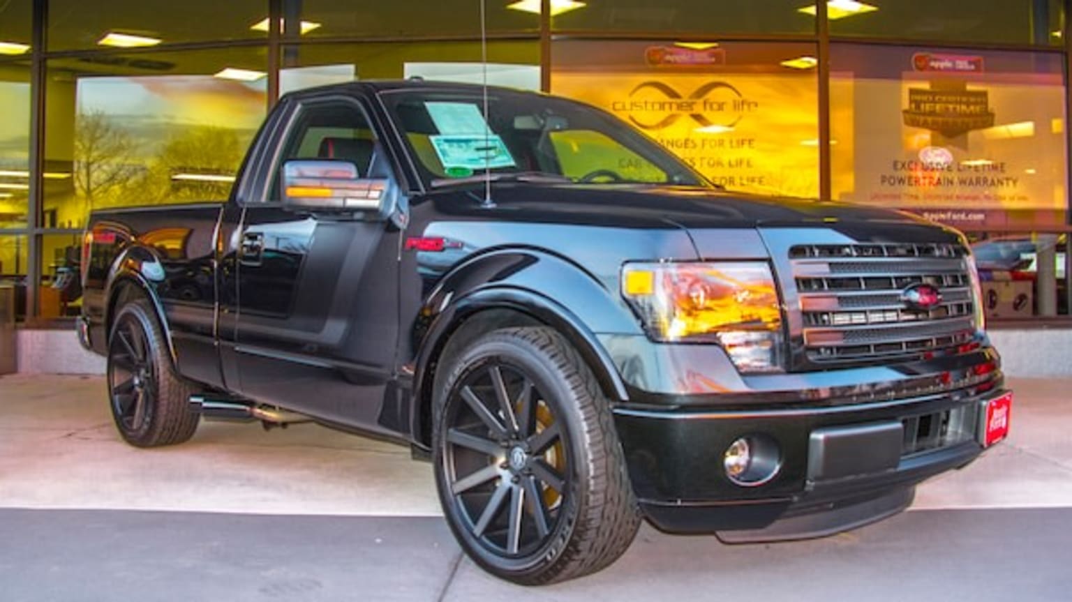 a black pickup truck parked in front of a store front window with a sign on the front of the truck