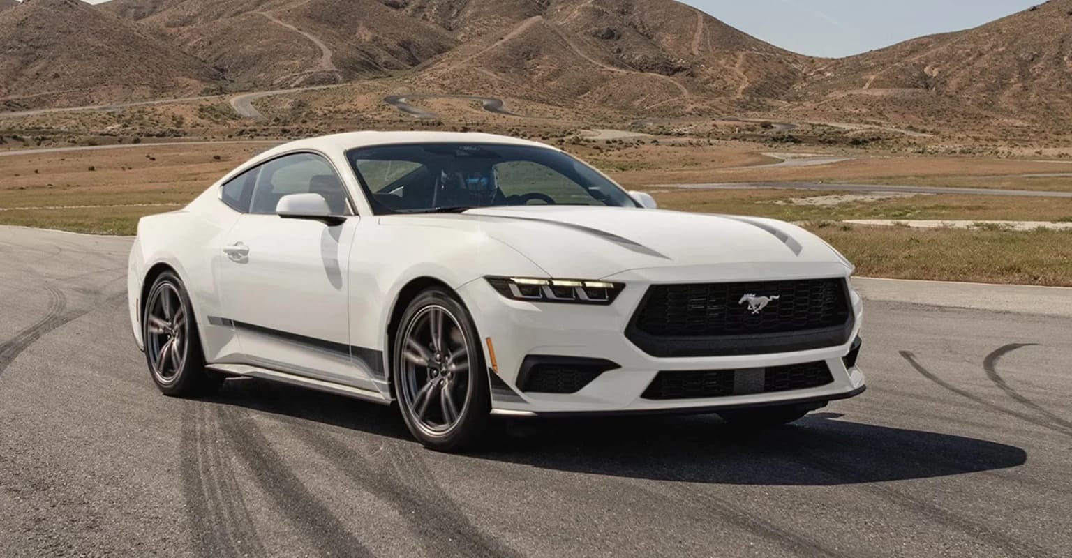 A sleek, white sports car is parked on a road with rugged, mountainous terrain in the background.