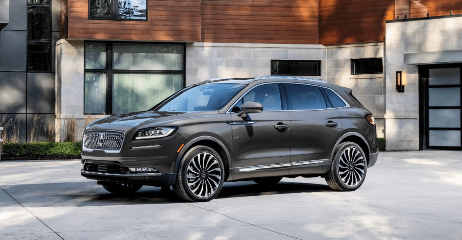 a grey lincoln suv is parked in front of a large building with a brown door and a black door handle