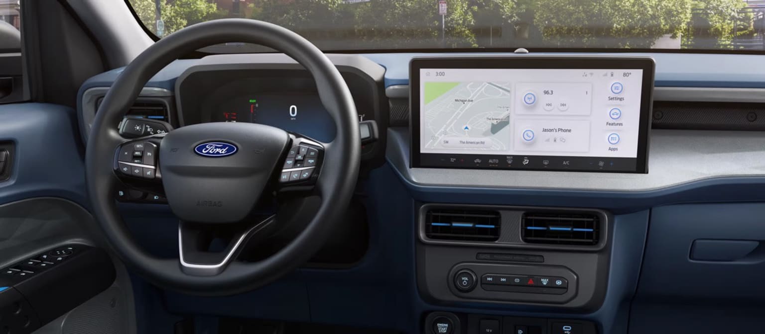 The image shows the interior of a vehicle, with a steering wheel and dashboard visible in the foreground, and a large display screen displaying a map in the background.