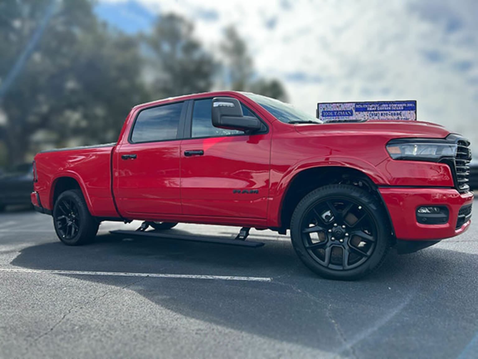 A red pickup truck with large tires and black accents parked on a paved road, trees and cloudy sky in the background.