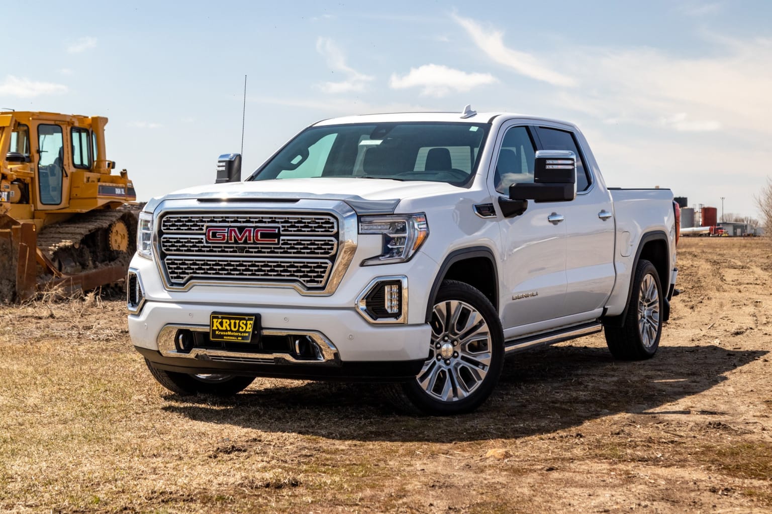 a white truck parked in a field next to a bulldozer and a truck on a dirt road