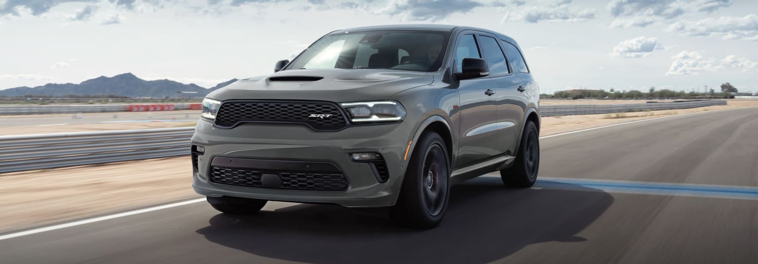 a gray dodge suv driving down a road with mountains in the background and clouds in the sky in the background