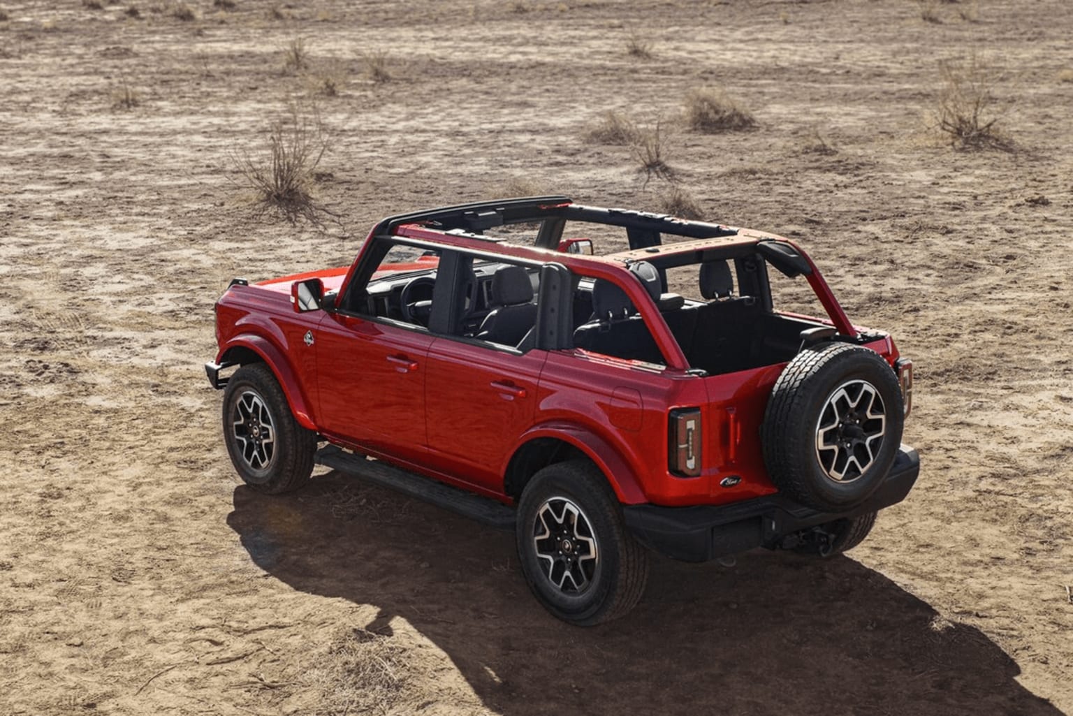 The image shows a red off-road vehicle with a rugged, boxy design parked in a dry, dusty landscape with sparse vegetation in the background.