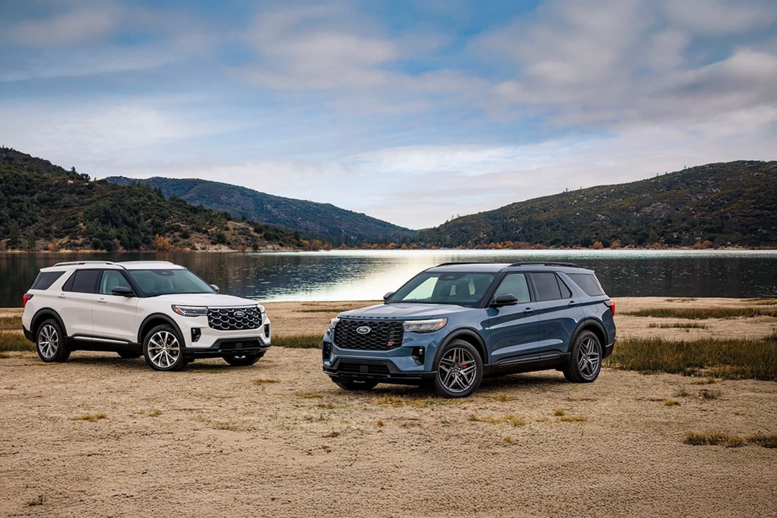 2025 Ford Explorer Platinum and 2025 Ford Explorer ST facing either other in front of mountain lake