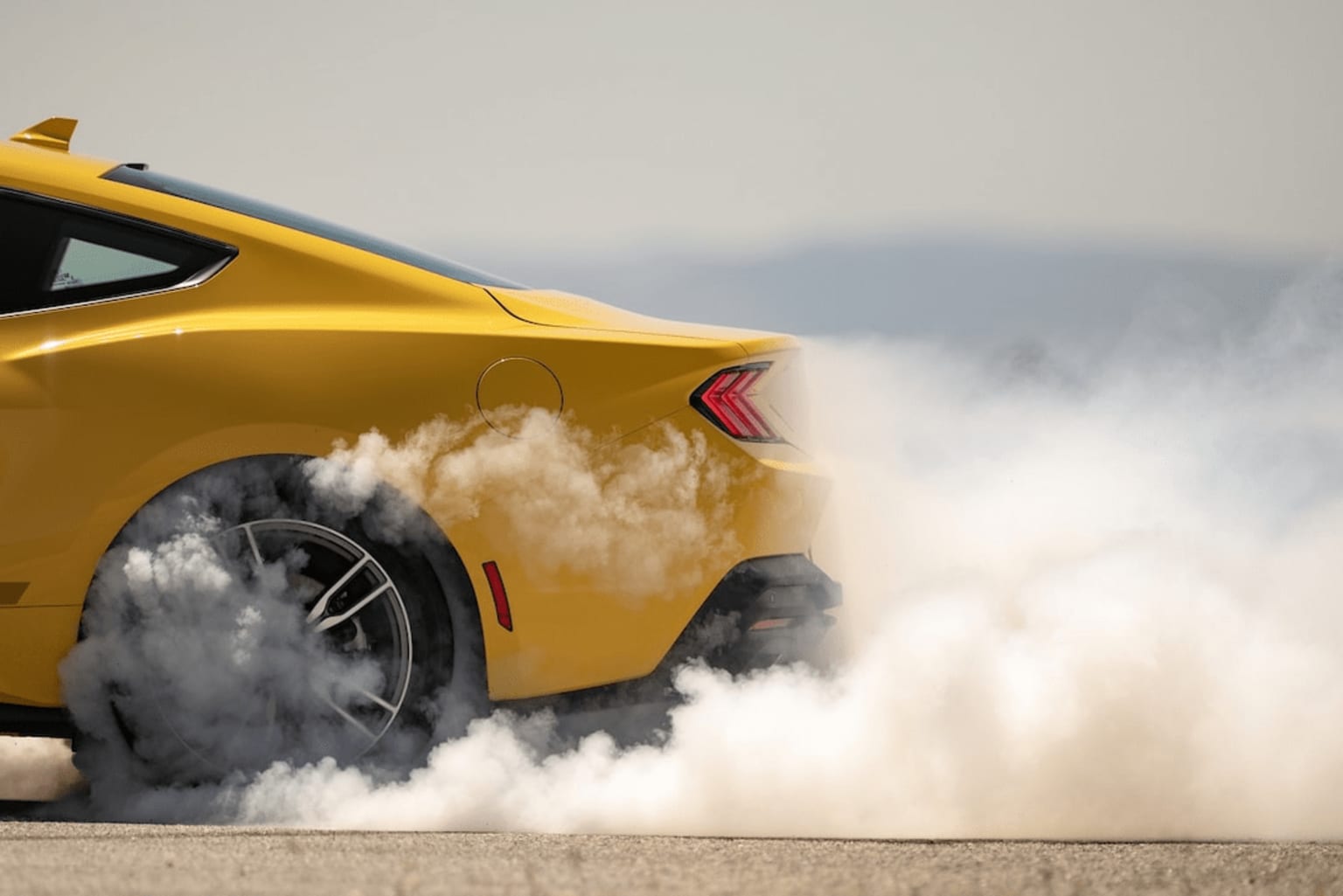 Yellow sports car with spinning wheels creating smoke and dust, blurred background.