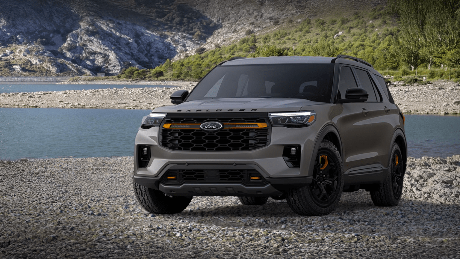 Grey SUV parked on rocky shoreline with lake and mountains in background.