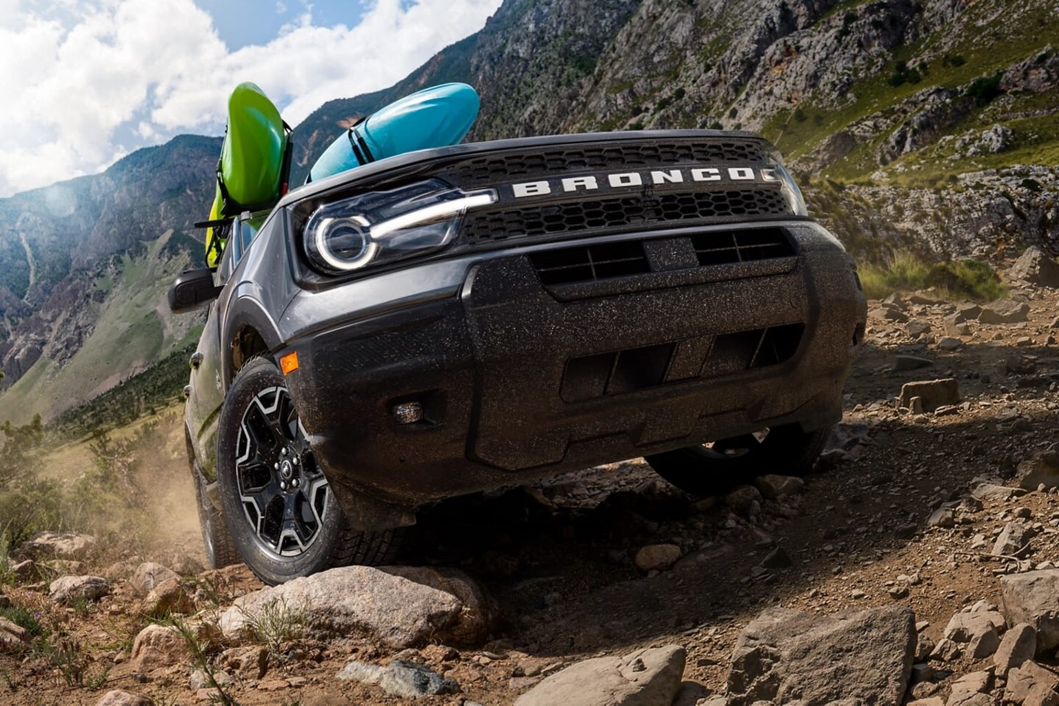 An off-road vehicle navigates a rocky, mountainous terrain with lush greenery and dramatic cliffs in the background.