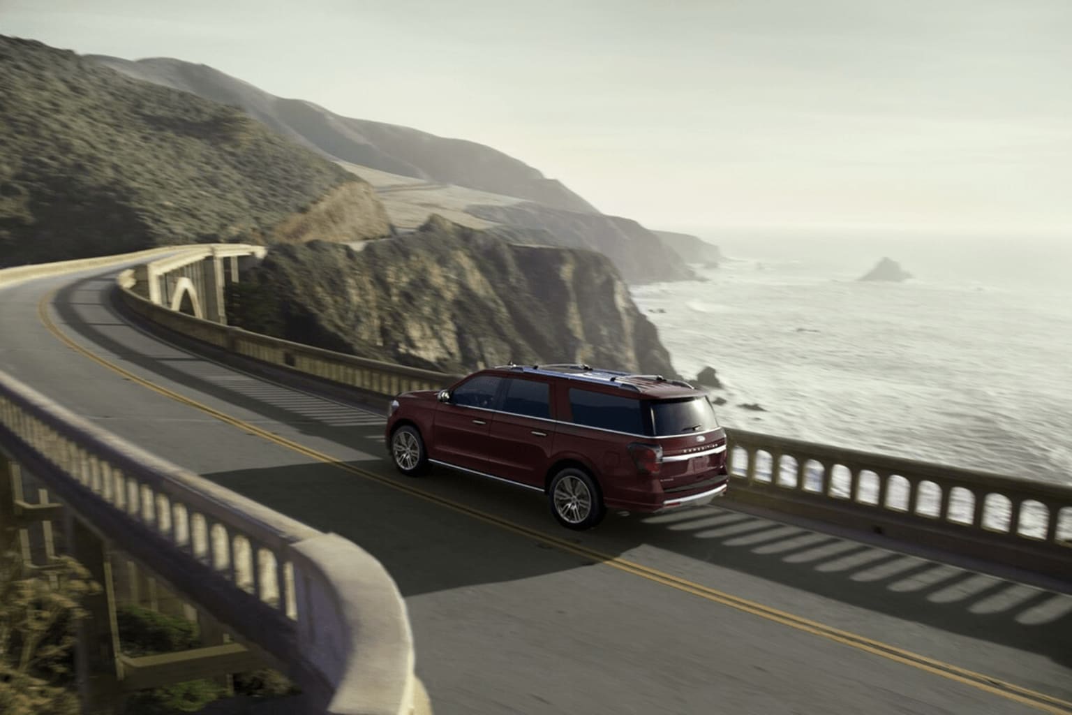 A red SUV driving on a winding coastal road with cliffs and ocean waves in the background.