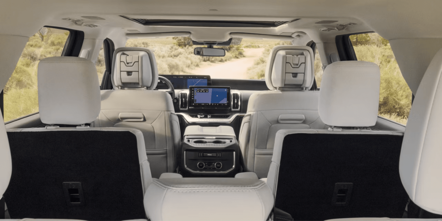 Interior of a modern SUV with white leather seats and a scenic view of a dirt road winding through a dry, grassy landscape.