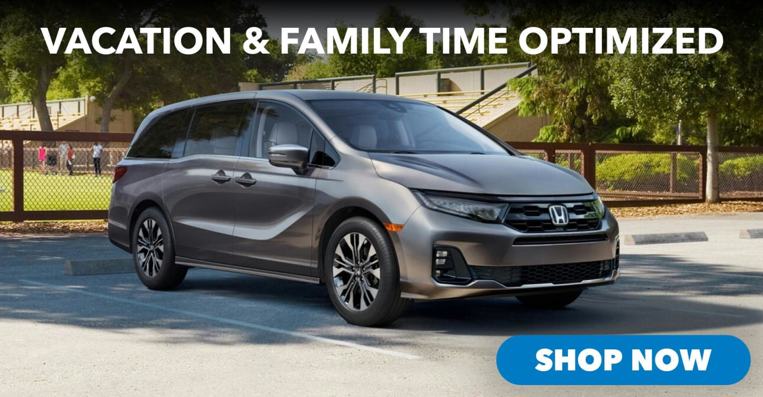A gray minivan parked in a lot with a family playing in the background.