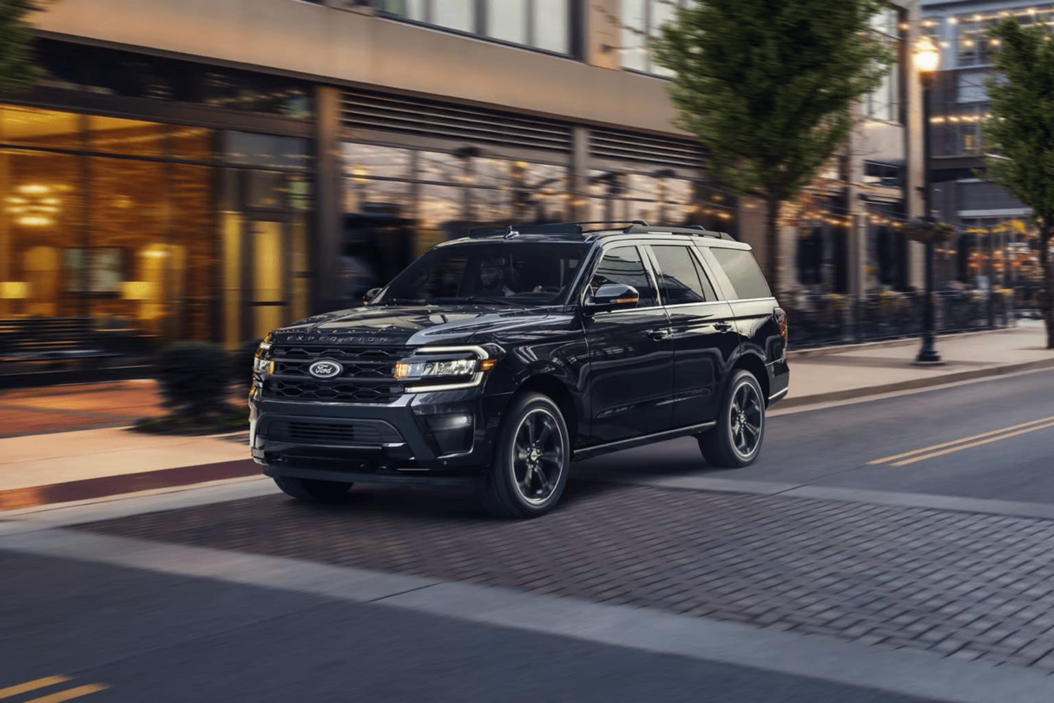 A large, black SUV parked on a city street with buildings and trees in the background.