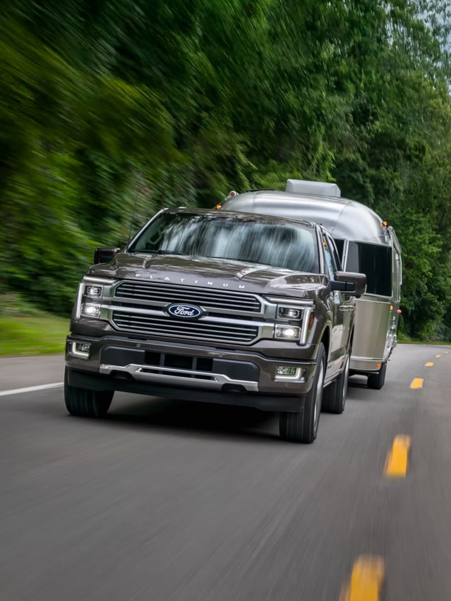 A large, silver SUV speeding down a road surrounded by lush, green foliage creating a blurred, dynamic background.