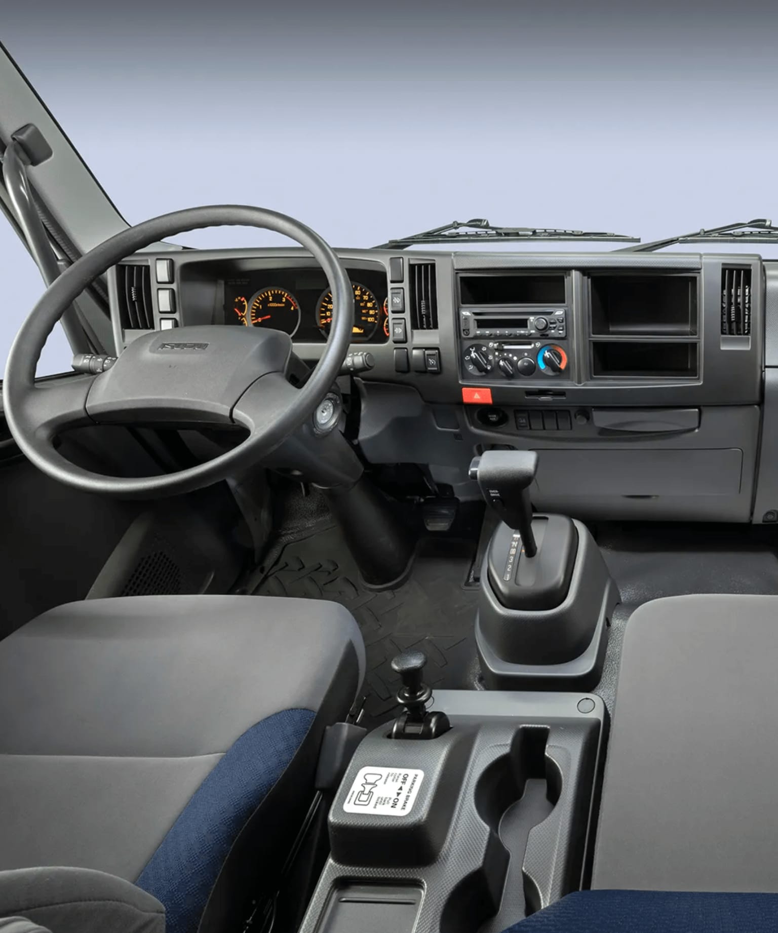 Grey truck interior with steering wheel and seats in foreground against light colored background through windshield
