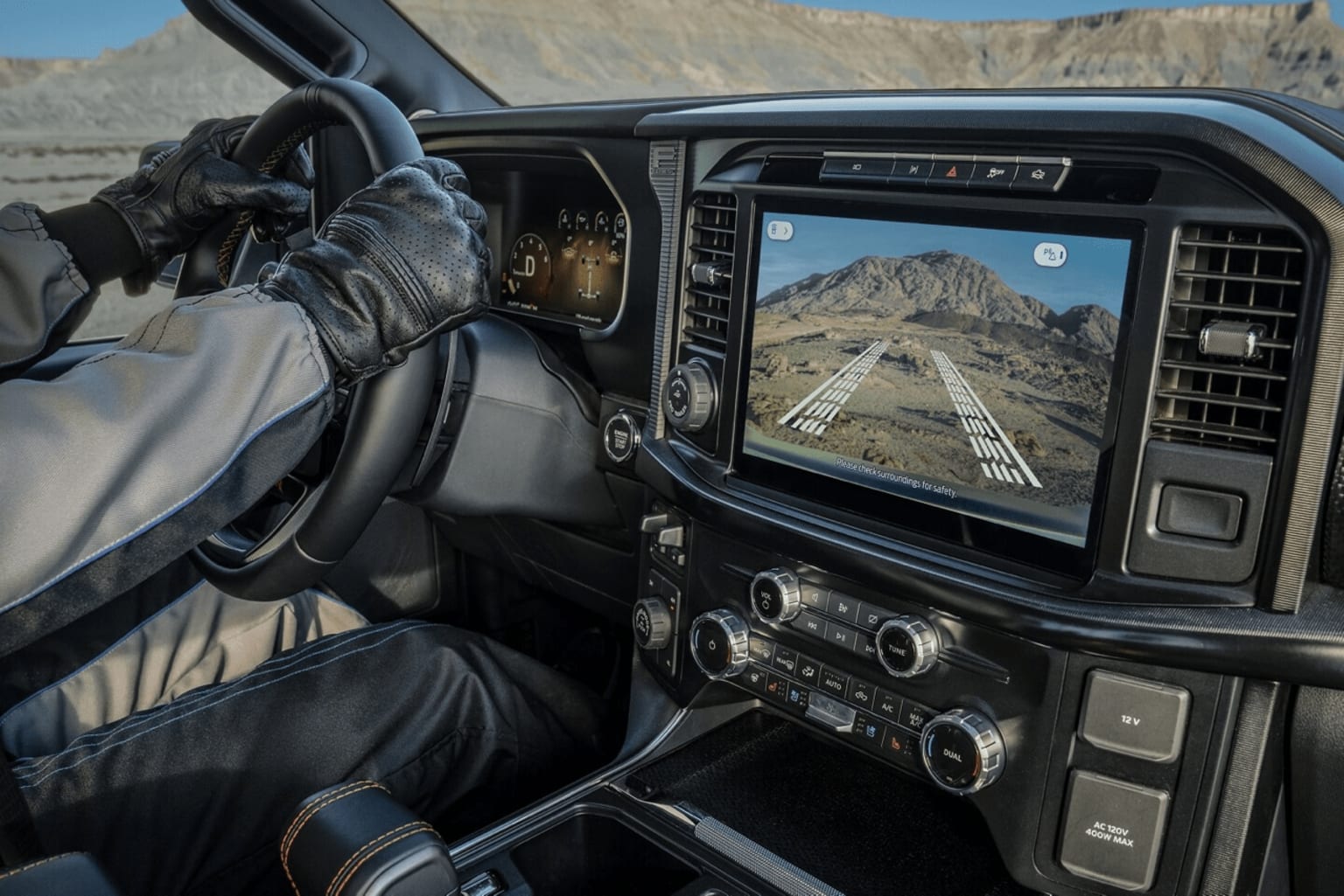 The image shows the interior of a vehicle with a dashboard display displaying a mountainous landscape in the background.