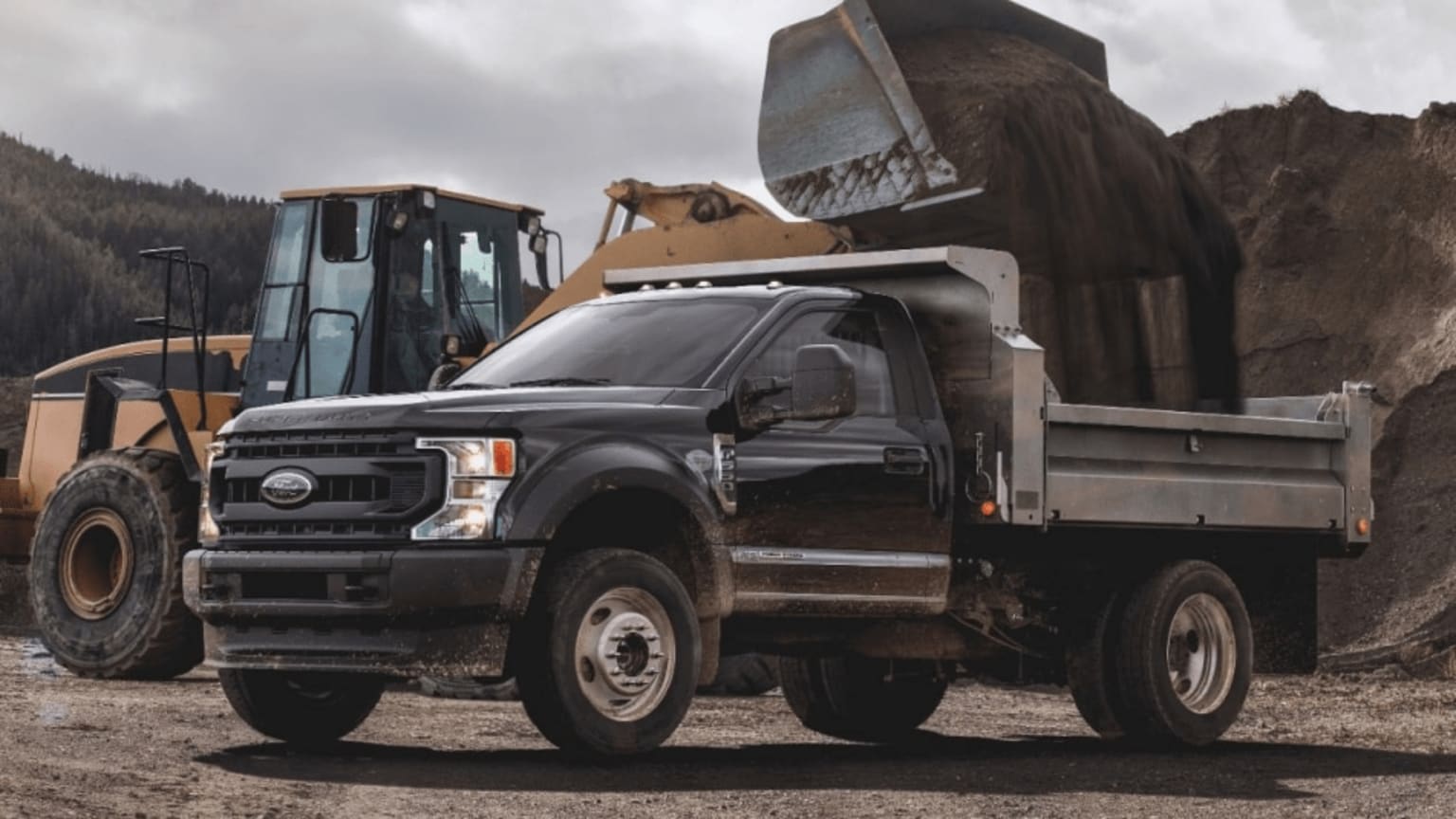 a dump truck parked in front of a pile of dirt and a bulldozer in the back of the truck