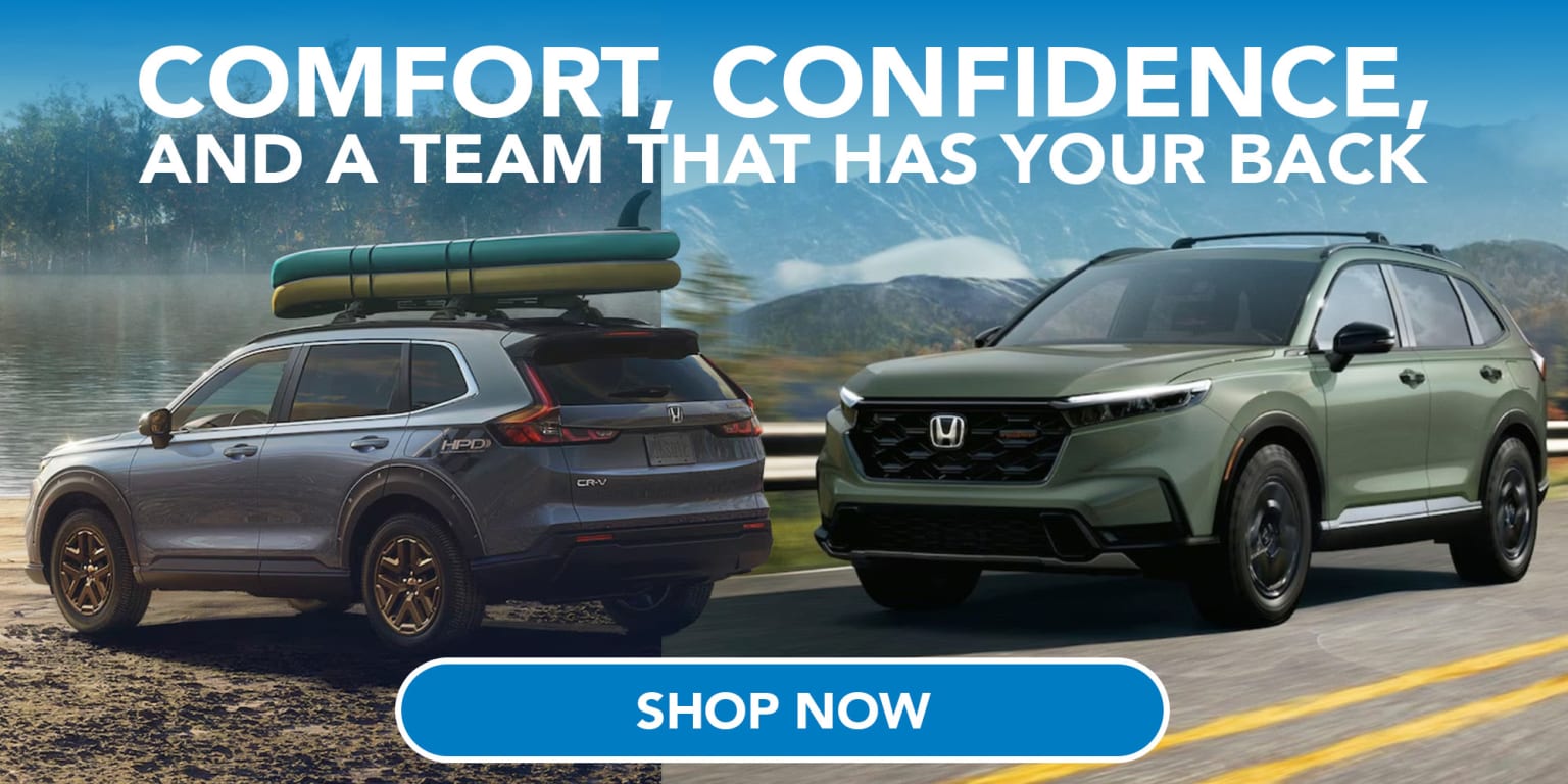 Two SUVs, one loaded with kayaks on its roof rack, are parked by a lake with mountains in the background.