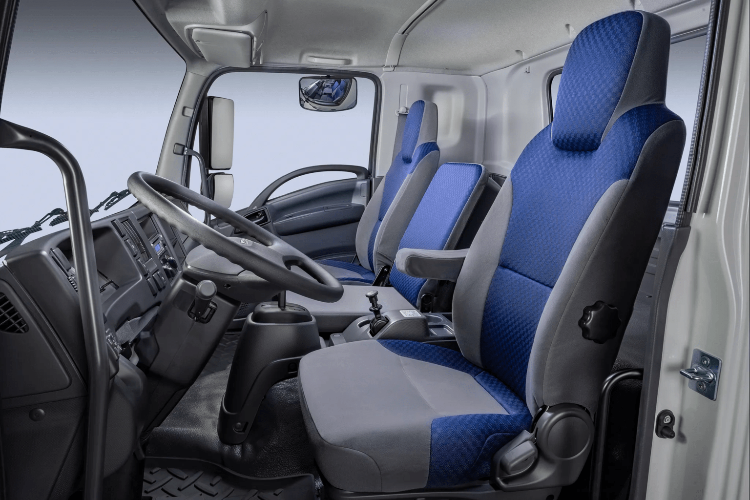 Blue and grey fabric seats occupy the foreground of a truck cabin, with a steering wheel and dashboard set against a light-colored interior background.