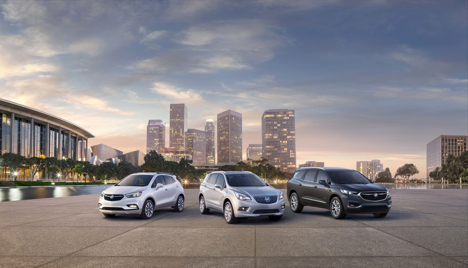 three vehicles parked in front of a cityscape at dusk with skyscrapers in the background