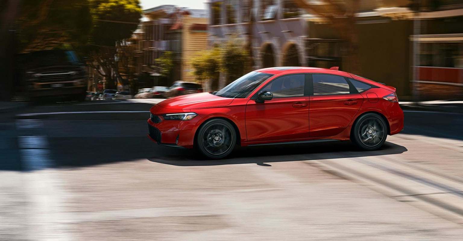 A red sedan speeding down a blurred street with buildings in the background.
