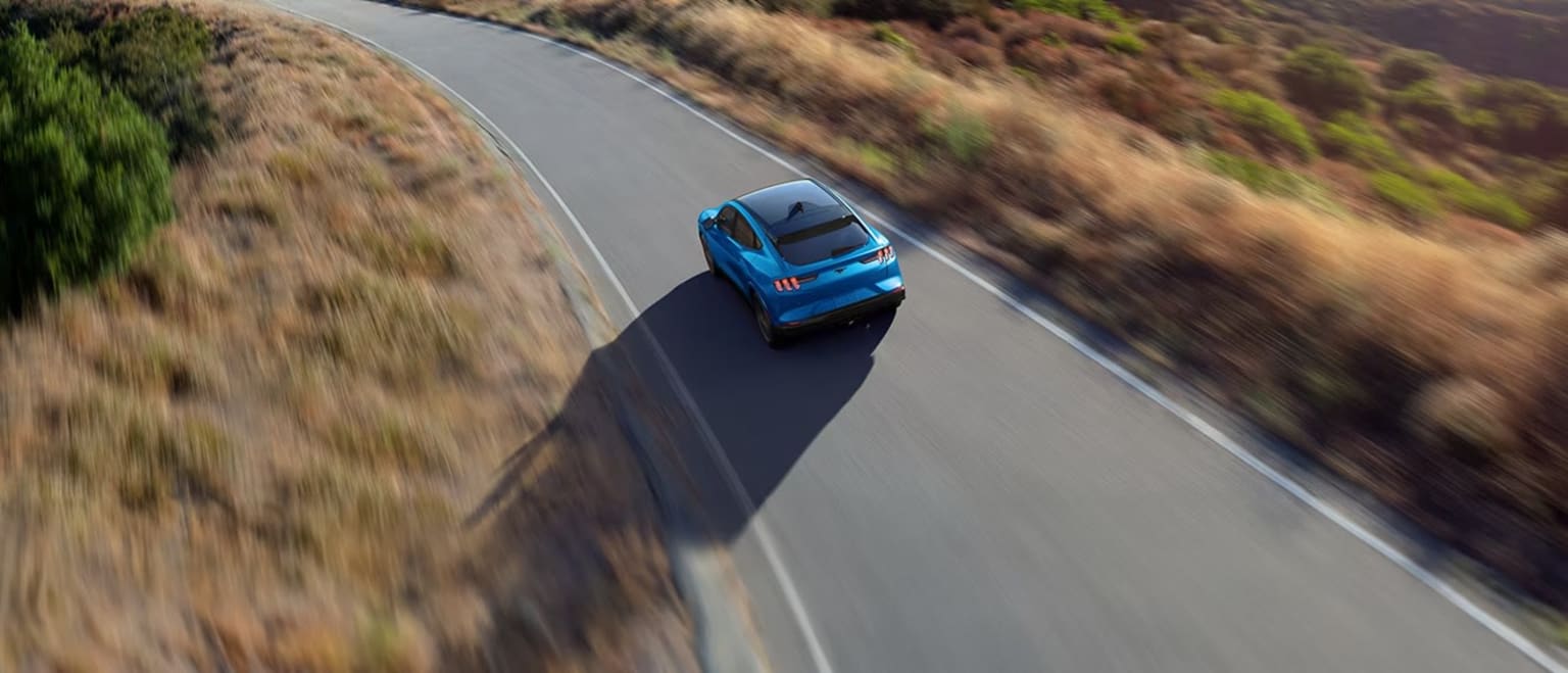 A blue car is speeding down a winding road surrounded by lush, blurred vegetation in the background.