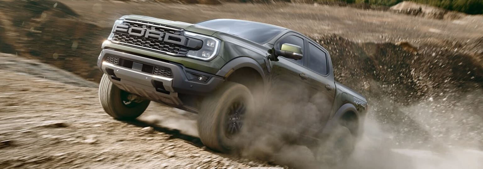 A rugged off-road truck speeding through a dusty, dirt-covered terrain, kicking up a cloud of dust in its wake.