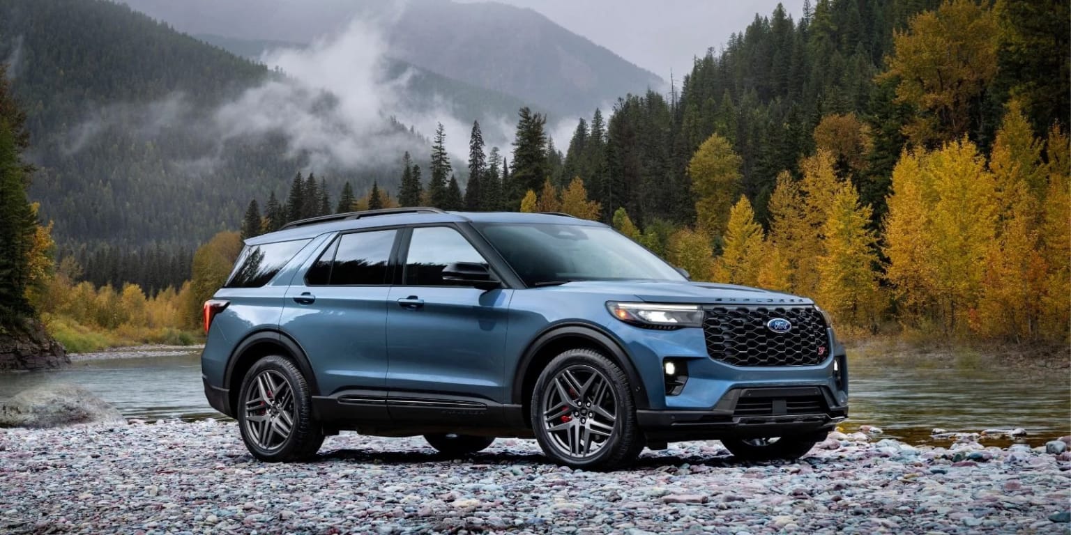 An off-road 2025 Ford Explorer in a mountain landscape with a rushing river, dense forests, and towering misty peaks.