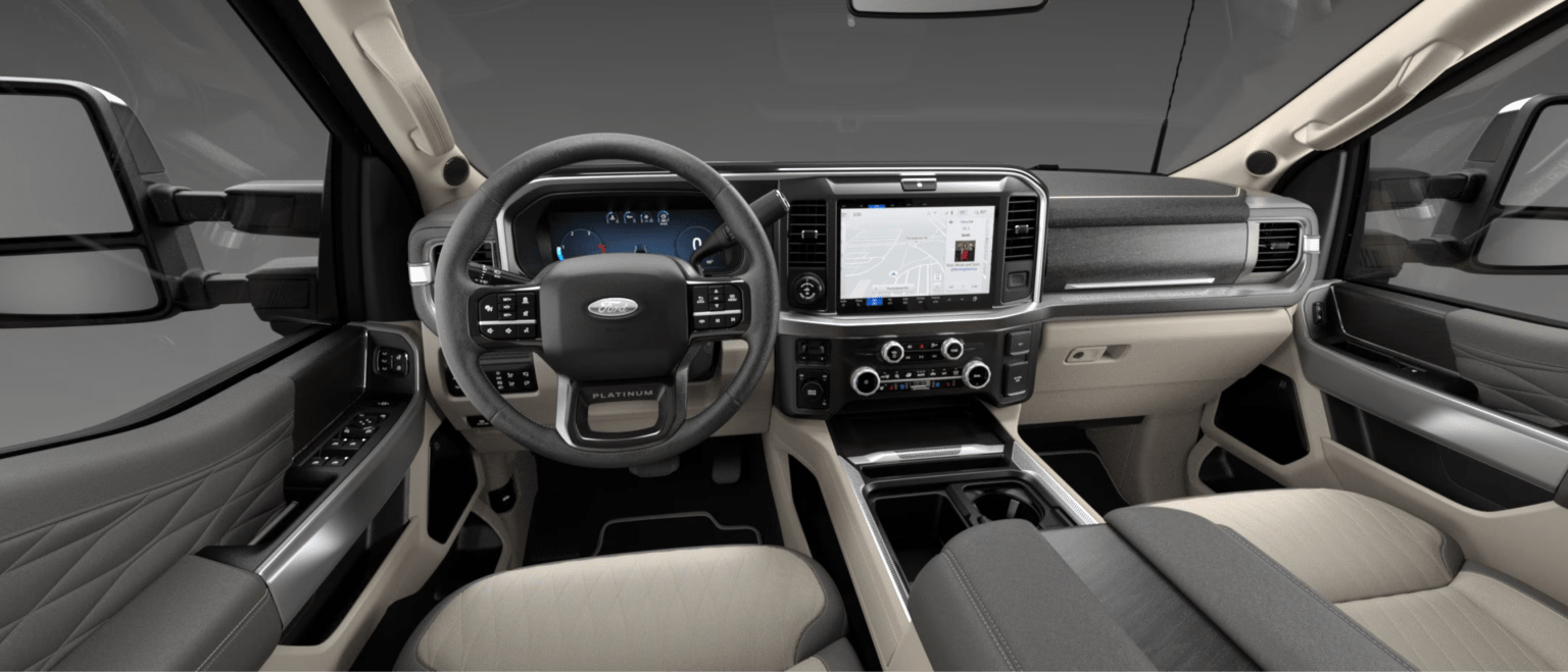 Modern truck interior with leather-wrapped steering wheel, digital dashboard, large infotainment screen, and light-colored seating.